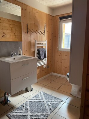 Ein Badezimmer mit Holzeinrichtung, einem Waschbecken mit Spiegel, einem Handtuchhalter und einem Fenster.