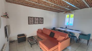 A living room with a sofa, a coffee table, a TV, and a dining area with a table and chairs.