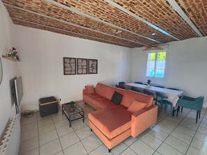 A living room with a sofa, a coffee table, a TV, and a dining area with a table and chairs.