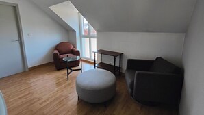 A loft-style room with a sloped ceiling, a brown leather armchair, a round ottoman, a dark sofa, and a small wooden table. - La Clef des Vignes 3 (Roye)
