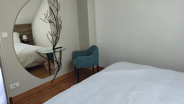 A bedroom with a bed, a chair, a round mirror, and a small table. - La Clef des Vignes 3 (Roye)