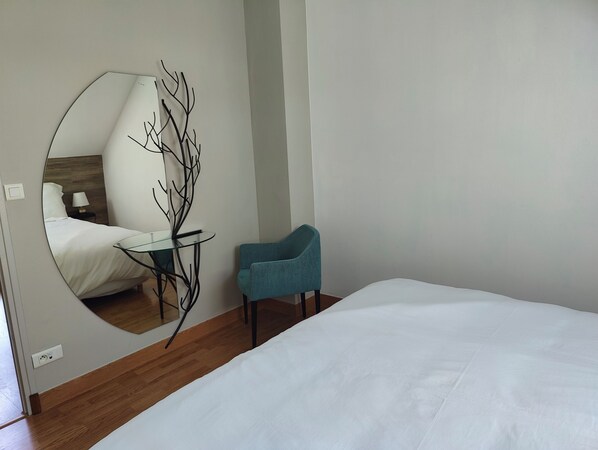 A bedroom with a bed, a chair, a round mirror, and a small table.
