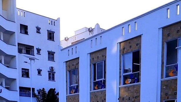 Una piscina con superficie de agua azul cristalina, rodeada por un edificio blanco con múltiples ventanas y balcones.