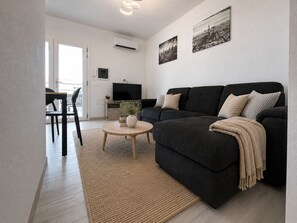 Ein modernes Wohnzimmer mit einem dunklen Sofa, einem runden Couchtisch und einem Fernseher.