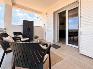 Un balcó amb zona d'estar, incloent cadires i una taula, i una porta corredissa de vidre que dona a un espai interior.