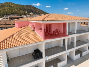 Un immeuble à plusieurs étages, doté d’un toit recouvert de tuiles rouges, de balcons et offrant une vue sur un paysage vallonné.