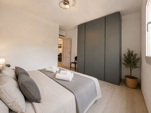 A modern bedroom with a bed, pillows, a bedside table, a lamp, a plant, and a wardrobe. - Alechri - Three Bedroom Apartment, Sleeps 5 (La Caletta)