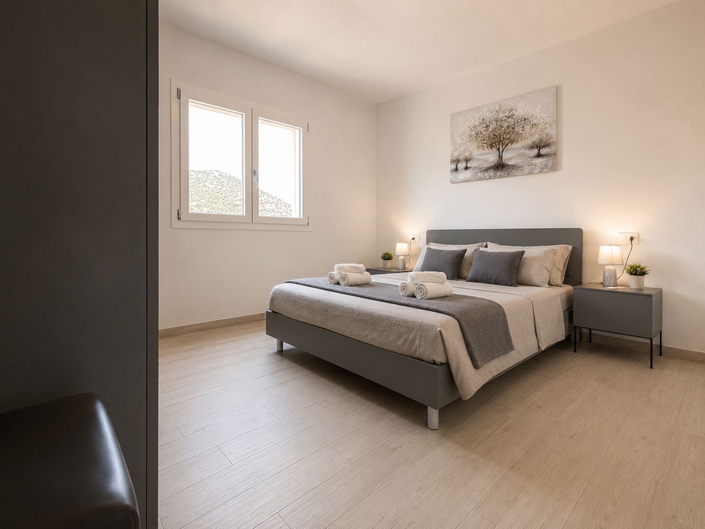 Une chambre à coucher moderne avec un lit, des tables de chevet, une fenêtre et un tableau au mur.