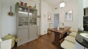 Ein Zimmer mit Holzboden, einem Esstisch, einer Vitrine und Wandbildern.