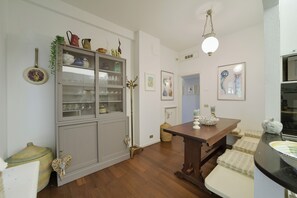 A room with a wooden floor, a dining table, a cabinet with glass doors, and wall-mounted artwork. - The Bay Garden Apartment- Santa Margherita Ligure (Santa Margherita Ligure)