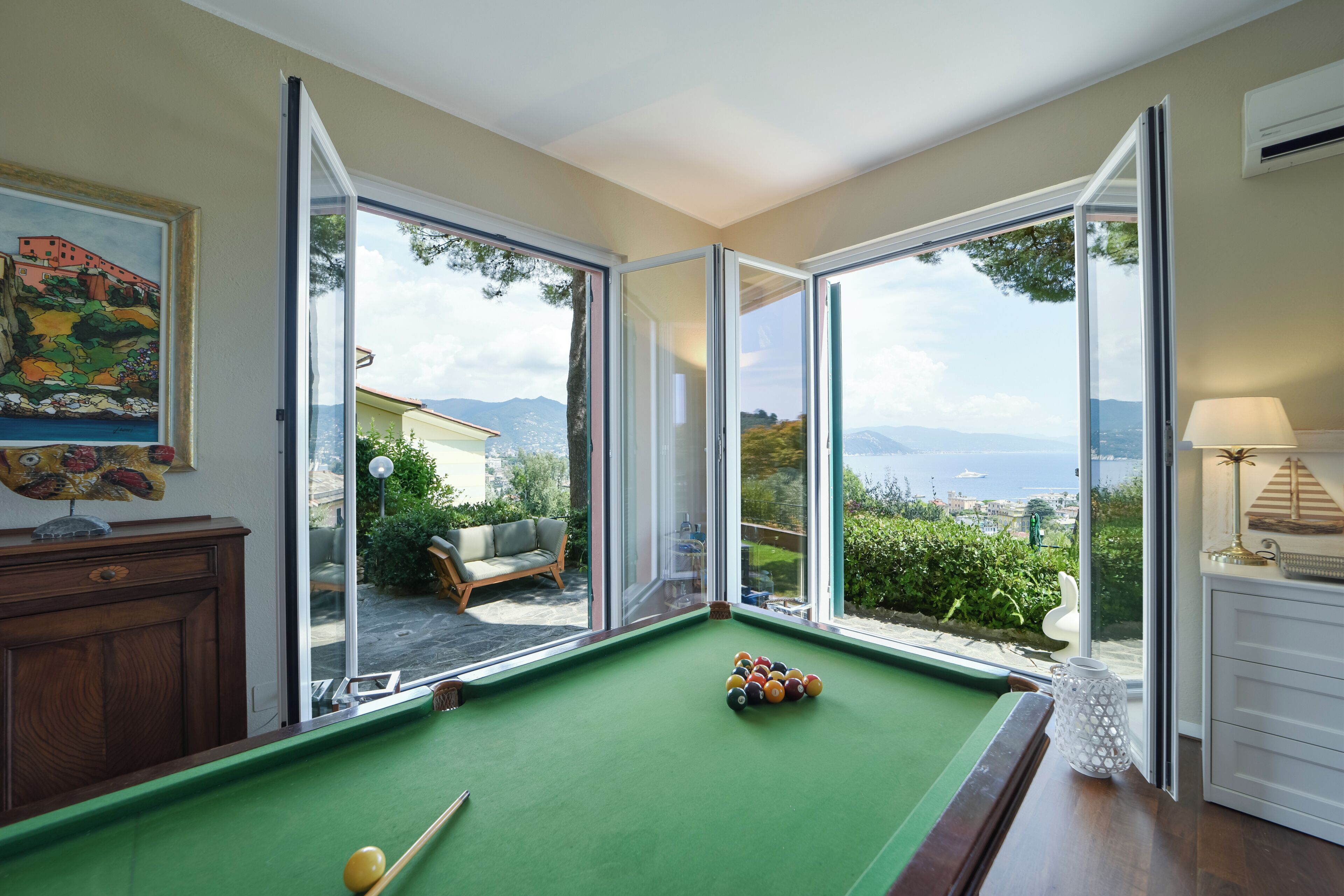 A pool table with a view of a hillside and a cityscape through large windows.