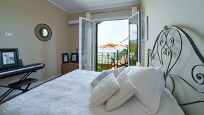 Ein Schlafzimmer mit einem Bett, einem Klavier, einem Spiegel und Blick auf einen Balkon mit Gartenmöbeln.