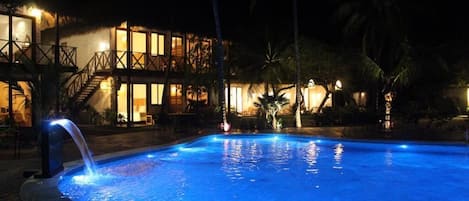 Piscina à noite com um edifício ao fundo.