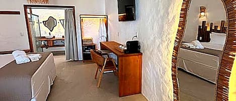 Una habitación de hotel con cama, escritorio, silla, espejo y televisor.