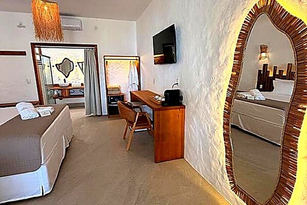 A hotel room with a bed, a desk, a chair, a mirror, and a television.