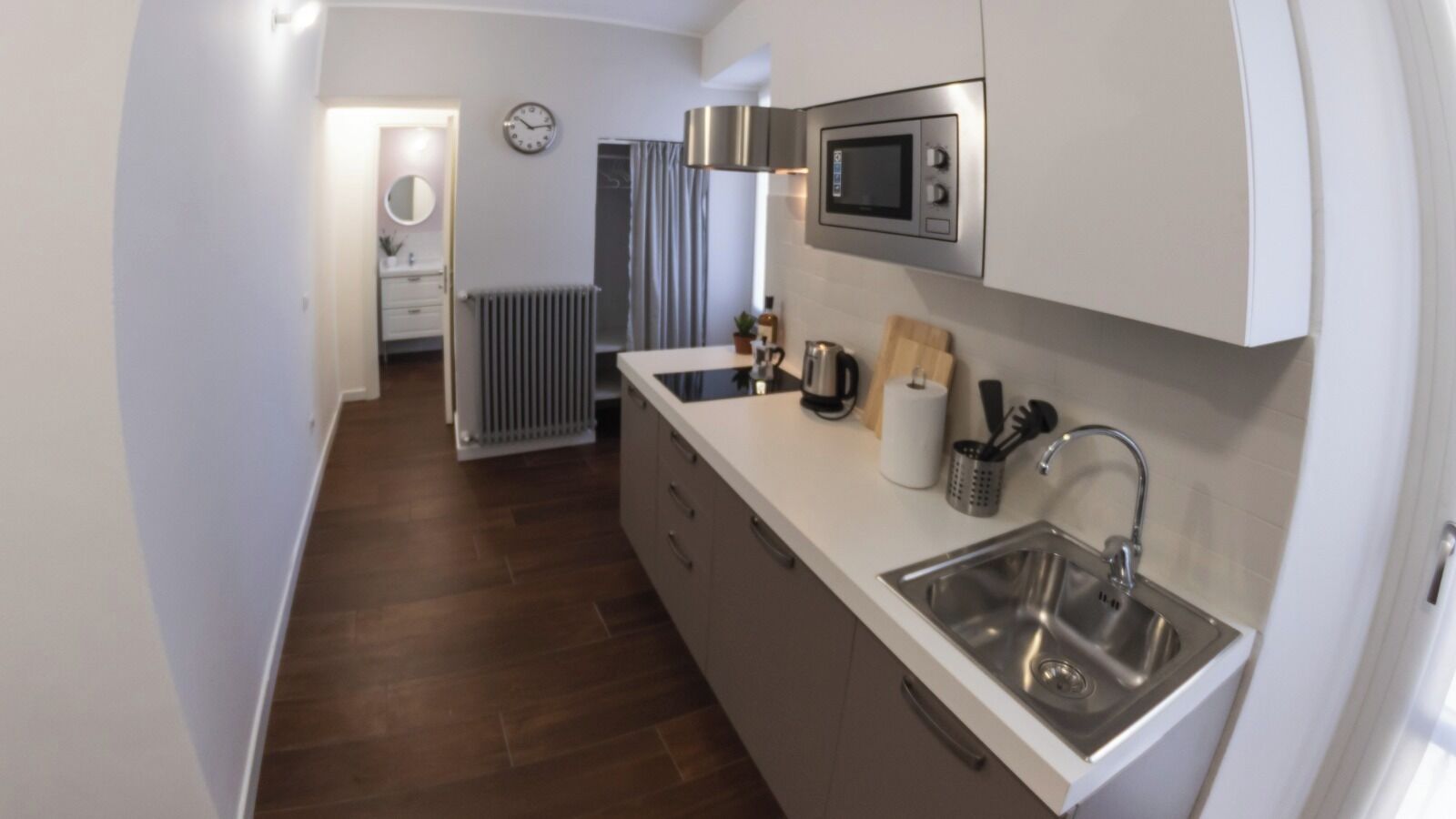 A compact kitchen with a microwave, sink, and wooden countertop.