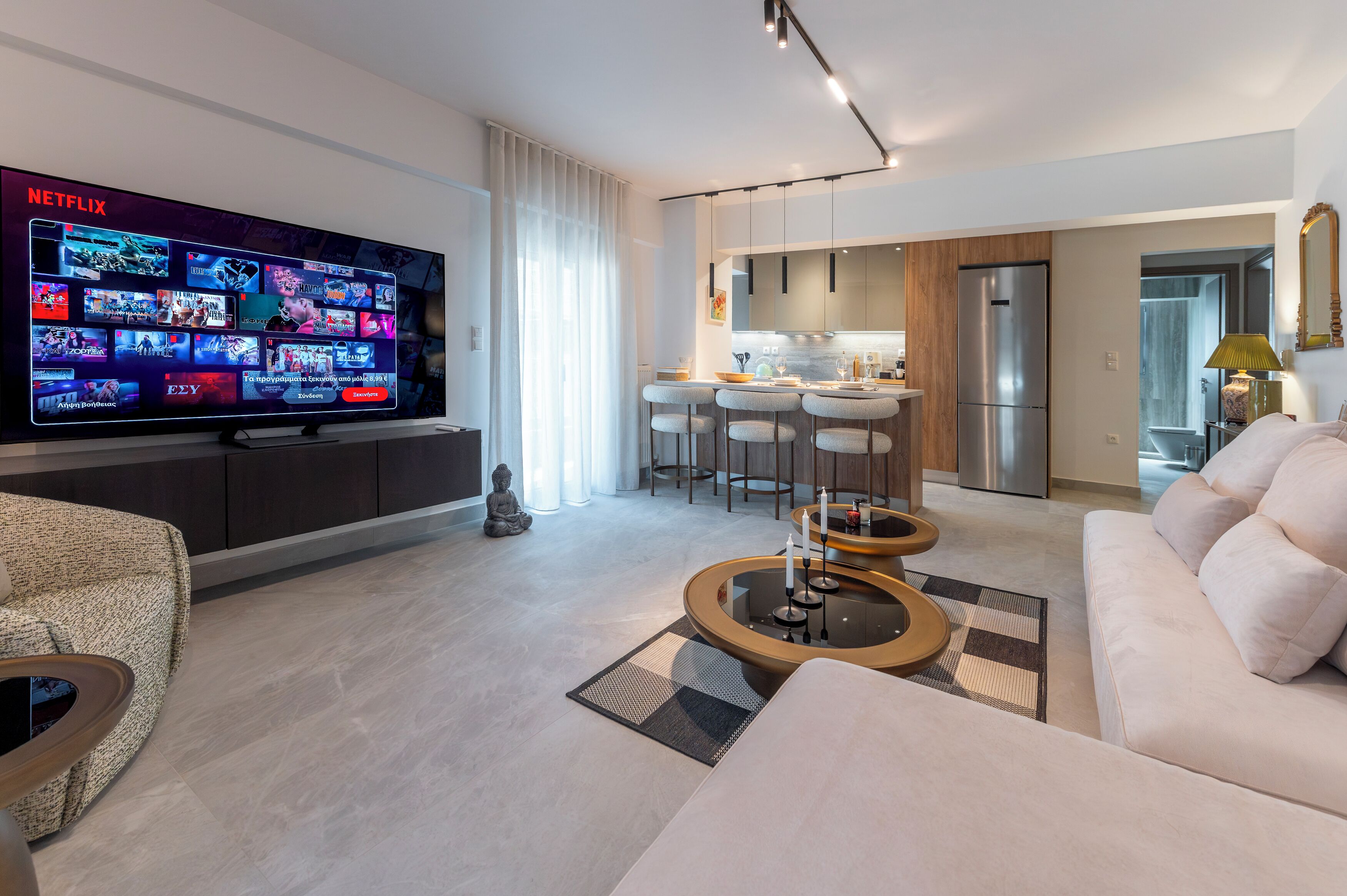 Uma sala de estar moderna com uma televisão de tela plana, um sofá, uma mesa de centro e uma área de refeições com banquetas.