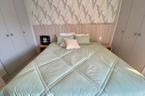 A bedroom with a bed, two nightstands, a mirror, and a wall with a leaf pattern. - SHB Apê incrível pé na areia (Santos)