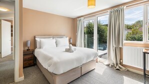 Ein Hotelzimmer mit einem großen Bett, einem Nachttisch, einer Lampe und Blick ins Freie.