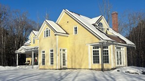 Ein gelbes Haus mit überdachter Veranda und Schornstein, umgeben von Schnee.