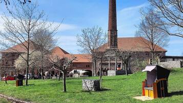 Un edificio histórico con una alta chimenea de ladrillo, muros de piedra y un patio cubierto de césped.