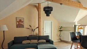 Een gezellige woonkamer met een hoekbank, twee ronde salontafels, een hanglamp en een eethoek met stoelen.