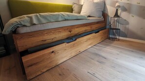 Een bed met houten frame en een groen hoofdeinde, een bedlampje en een muur met een bladmotief.