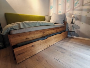 A bed with a wooden frame and a green headboard, a bedside lamp, and a wall with a leaf pattern. - Wellness-apartment mit Eigener Sauna und Whirlpool (Grossharthau)