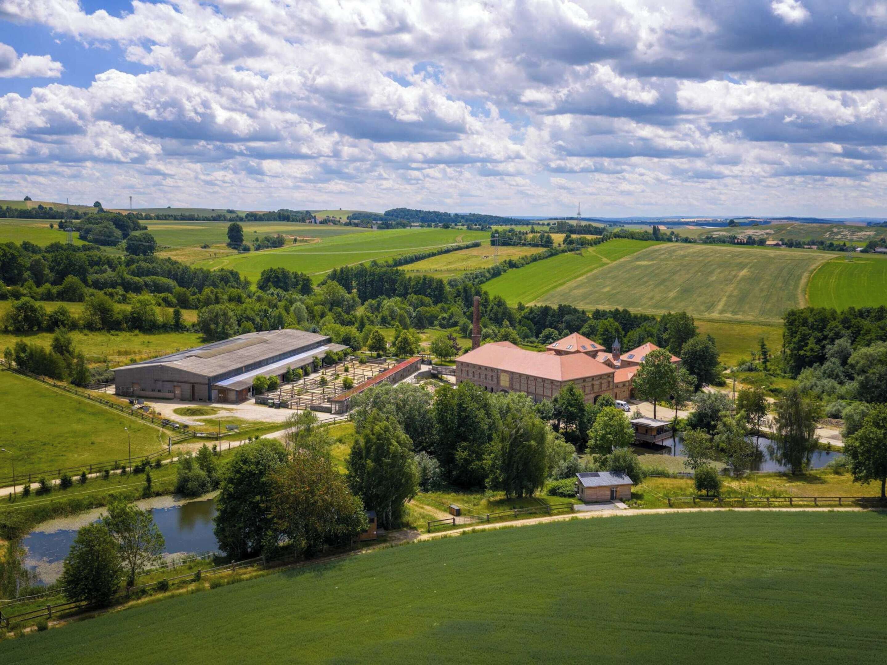 Paisagem rural com um grande celeiro, uma construção menor e um lago.