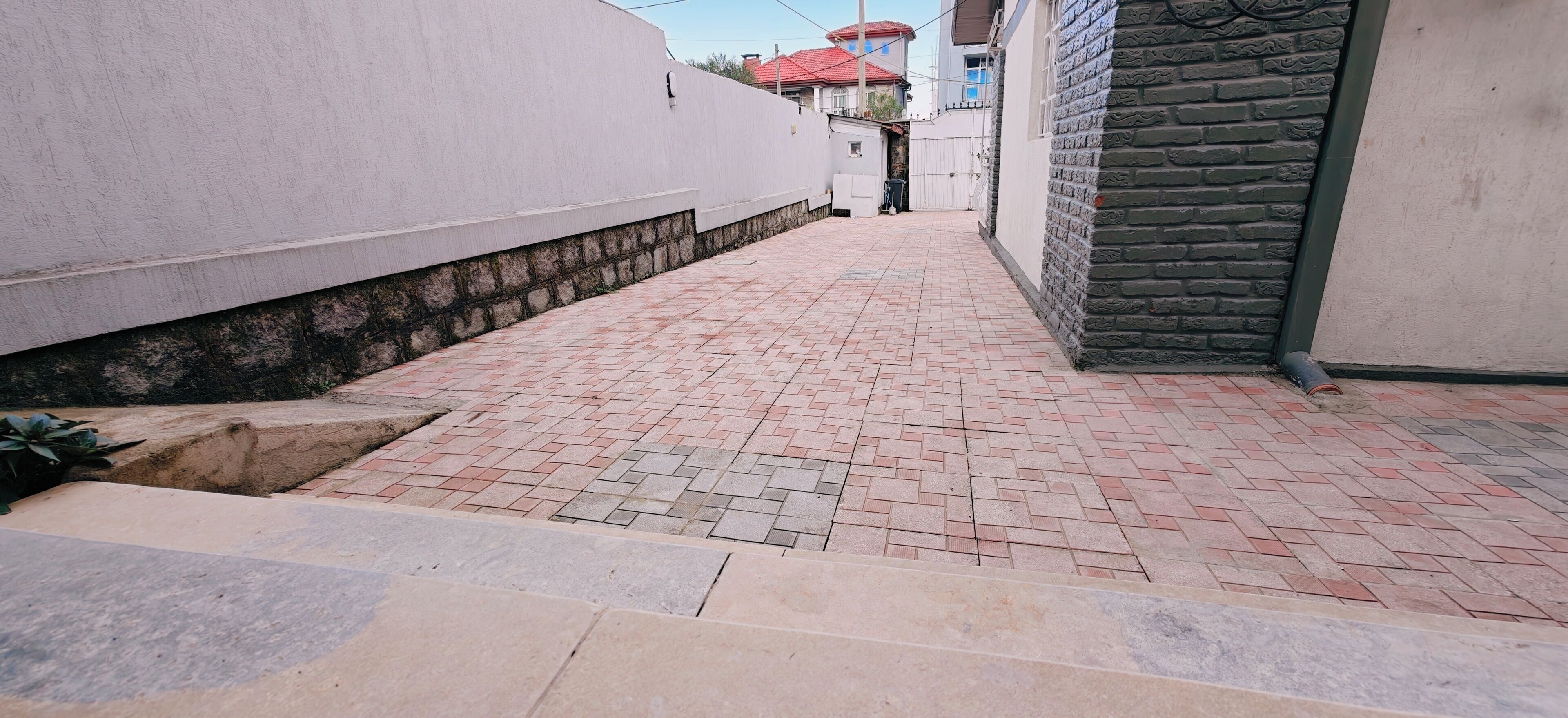 A narrow alleyway with a brick pathway, a stone wall on one side, and a building with a brick facade on the other.