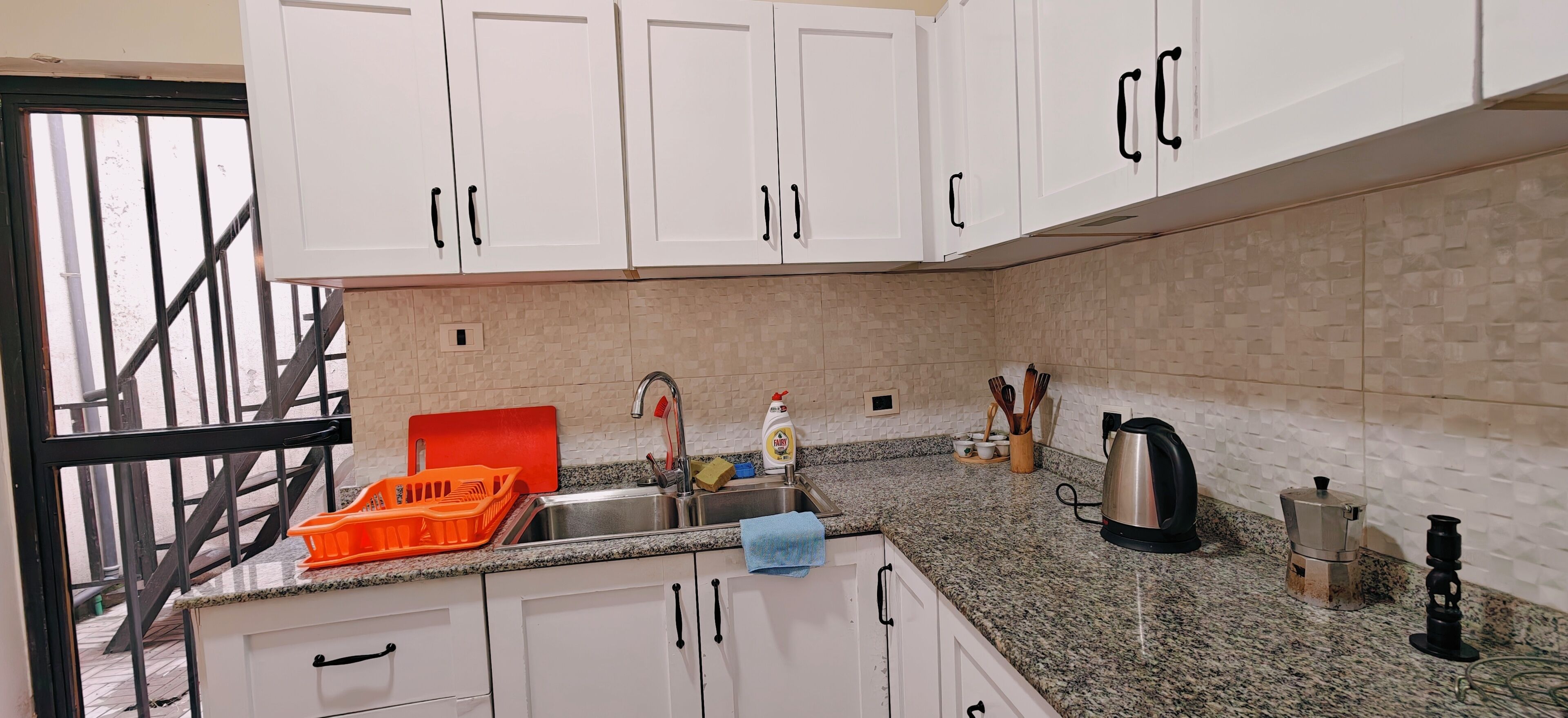 A kitchen with white cabinets, a granite countertop, a stainless steel sink, and various kitchen utensils.