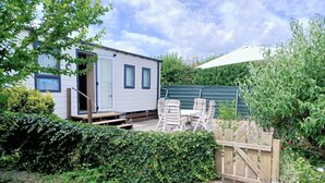 Ein Mobilheim mit Terrasse, Sitzgelegenheiten im Freien und einem Garten.