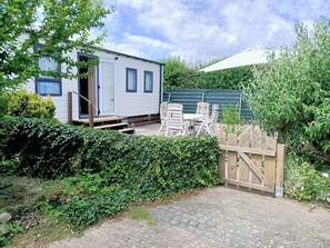 Ein Mobilheim mit Terrasse, Sitzgelegenheiten im Freien und einem Garten.