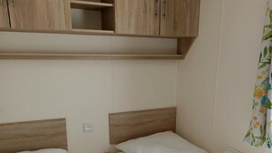 Ein Zimmer mit zwei Betten, Holz-Kopfteilen und einem fest installierten Regal über den Betten.