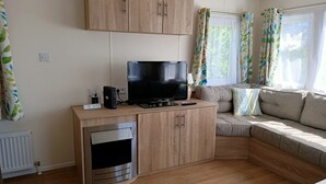 Ein modernes Wohnzimmer mit Flachbildfernseher, Holzsäcken, Backofen und einer Couch mit Kissen.