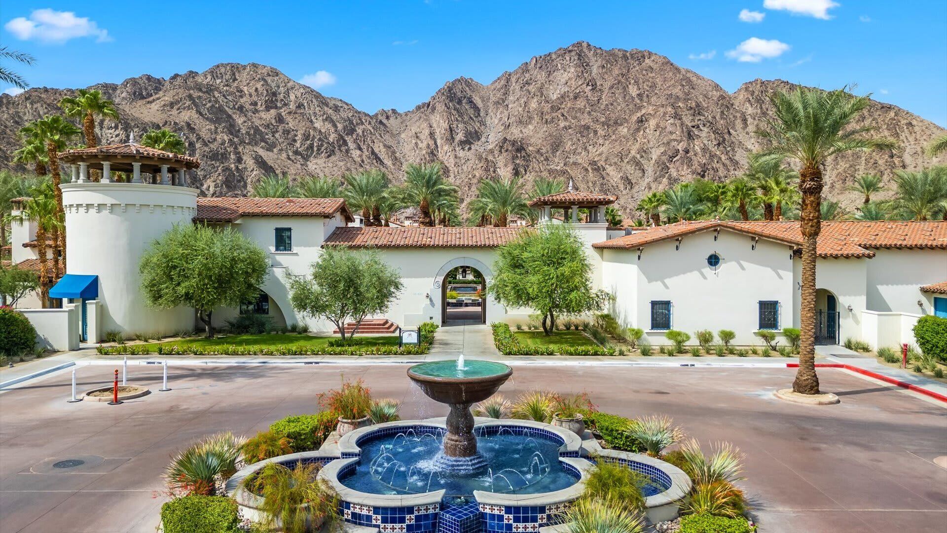 A courtyard with a fountain, palm trees, and a view of mountains.