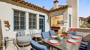 An outdoor patio with a dining table set for four, surrounded by wicker furniture and blue cushions. - LV307 3BR-3BA Legacy Villas Gem with Mountain Views (La Quinta)