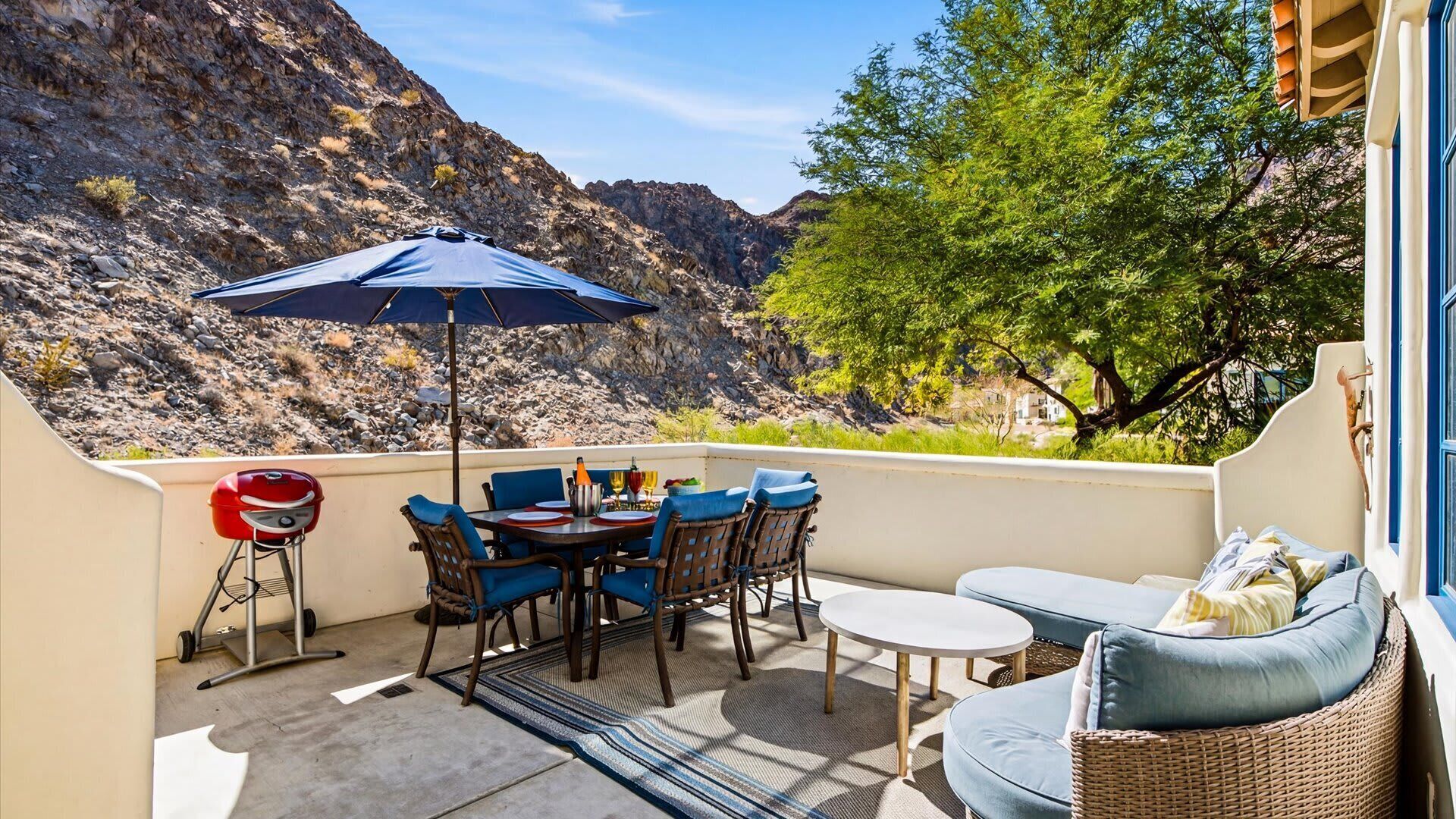 Une terrasse avec une table, des chaises, un barbecue et un parasol.