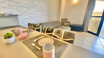 Una sala de estar moderna con un sofá, una mesa de comedor dispuesta con platos, tazas y cubiertos, y una planta en maceta.