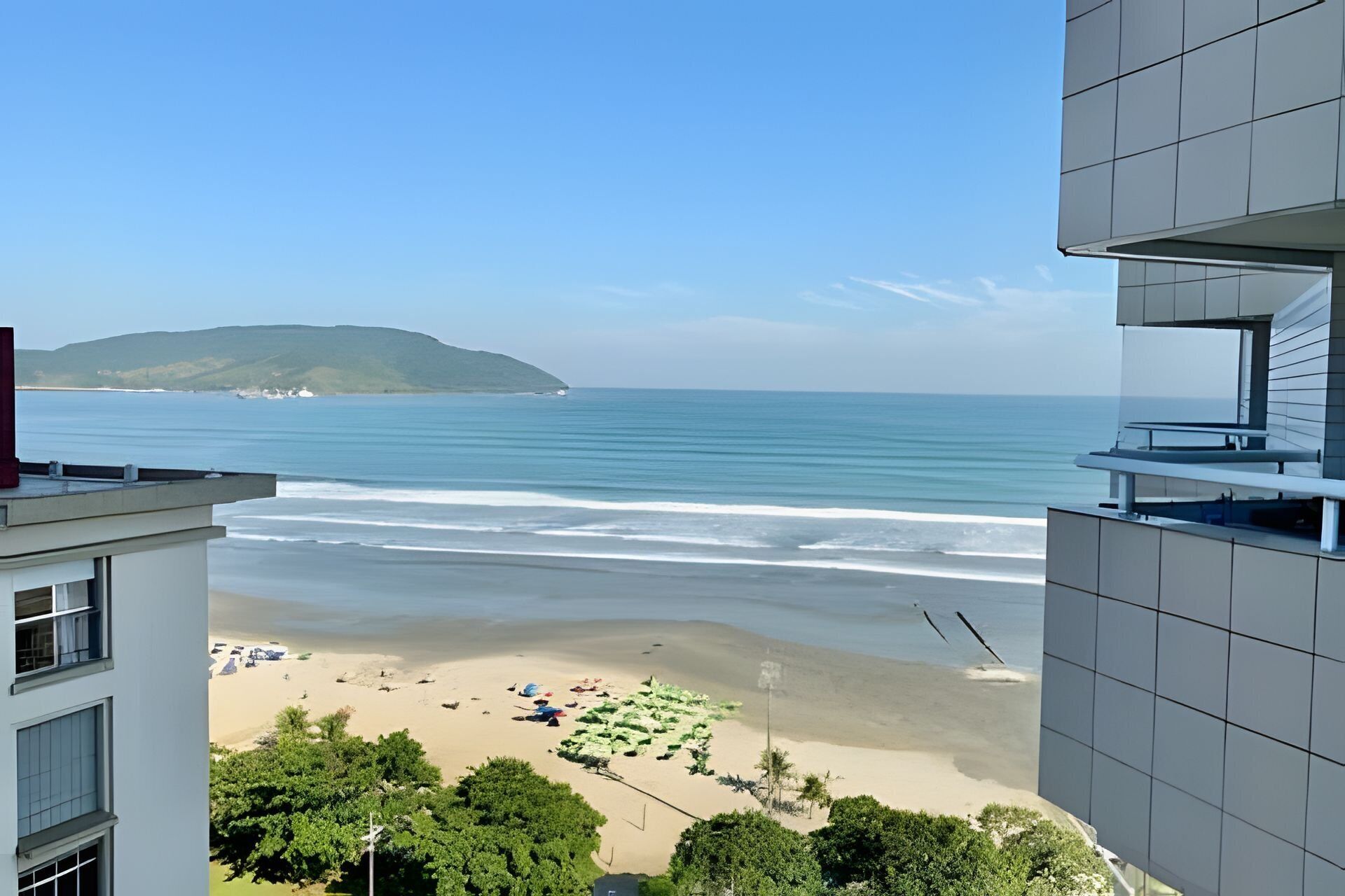 A view of a beach from a building with a balcony overlooking the ocean and a distant island.