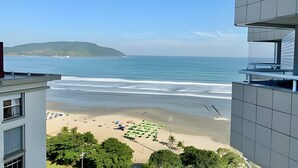 A view of a beach from a building with a balcony overlooking the ocean and a distant island. - SHB Lindo apartamento frente a praia (Santos)