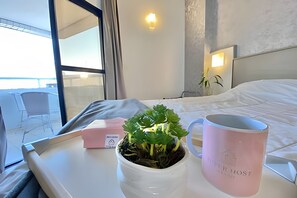 A hotel room with a bed, a bedside table with a potted plant and a pink mug, and a window with a view of the outside. - SHB Lindo apartamento frente a praia (Santos)