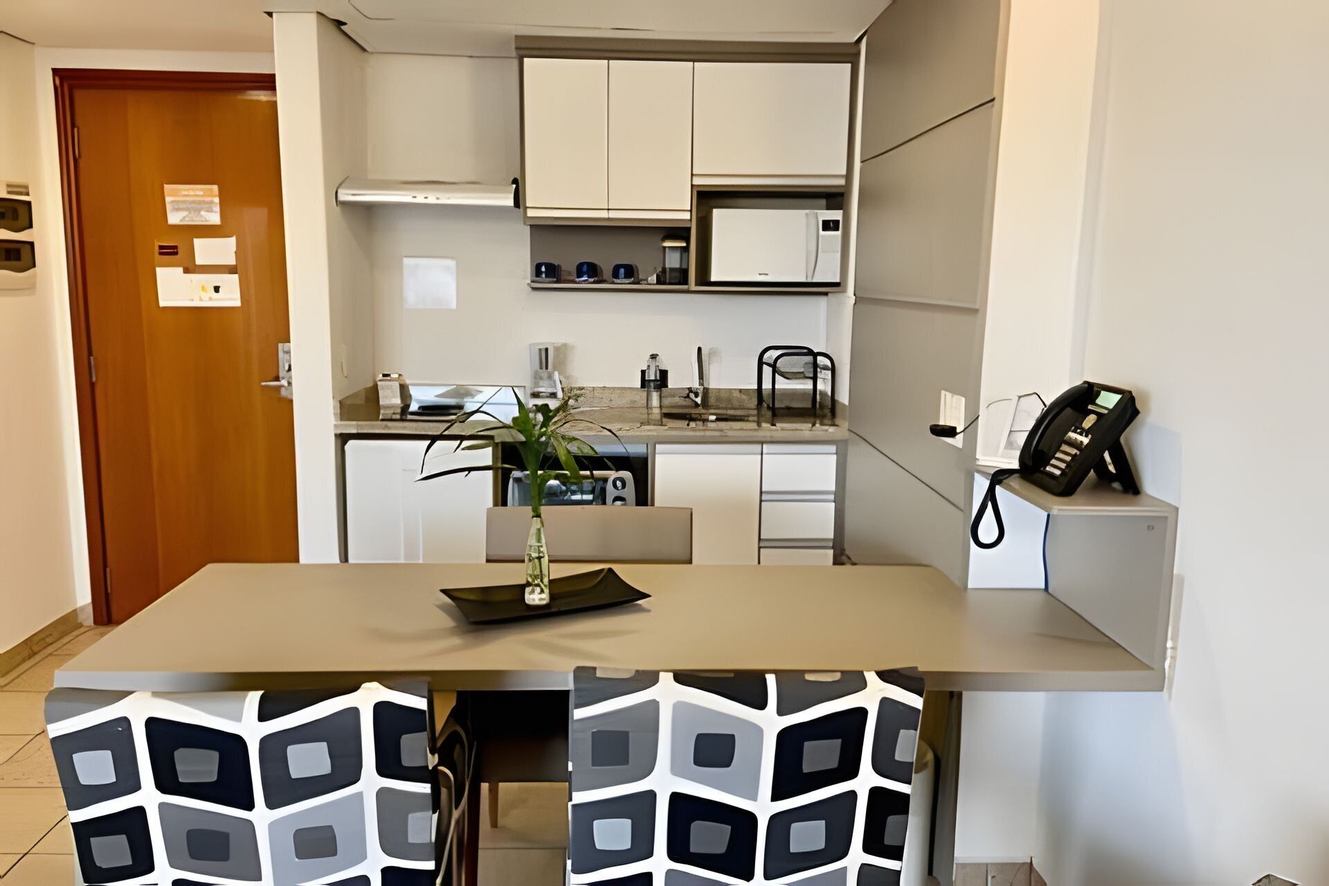 A compact kitchen with white cabinets, a refrigerator, a coffee maker, and a phone on a shelf.
