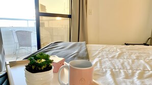 A neatly made bed with a white comforter and a pink mug on a bedside table. - SHB Lindo apartamento frente a praia (Santos)