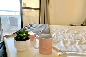 Ein ordentlich bezogenes Bett mit weißer Decke und einer pinken Tasse auf einem Nachttisch.