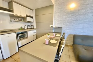 A modern kitchen with a dining area, featuring a built-in oven, microwave, and a small island with a sink. - SHB Lindo apartamento frente a praia (Santos)