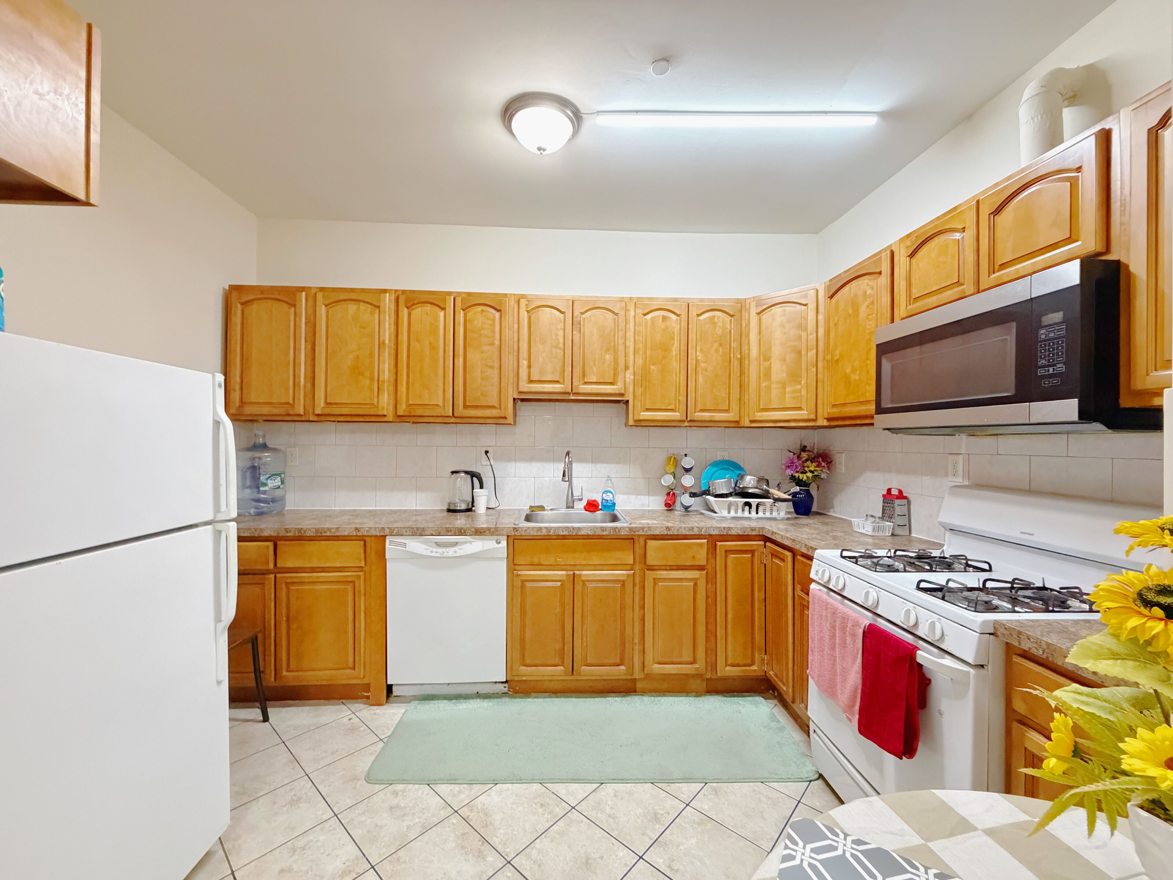 A kitchen with wooden cabinets, a white refrigerator, a dishwasher, a microwave, a stove, and a sink.