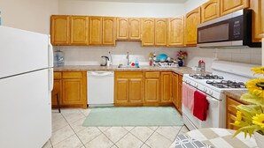 A kitchen with wooden cabinets, a white refrigerator, a dishwasher, a microwave, a stove, and a sink. - Beautiful Private room in a  2-bedroom apartment in vibrant Jersey City (Jersey City)
