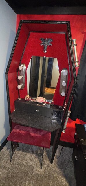 A room with a red and black themed decor, featuring a mirror, a small bench, and a decorative item on the wall.