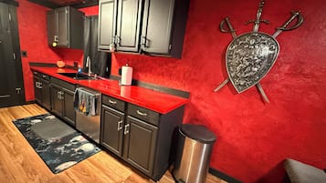 Cocina con armarios oscuros, encimera roja y escudo decorativo con espadas.